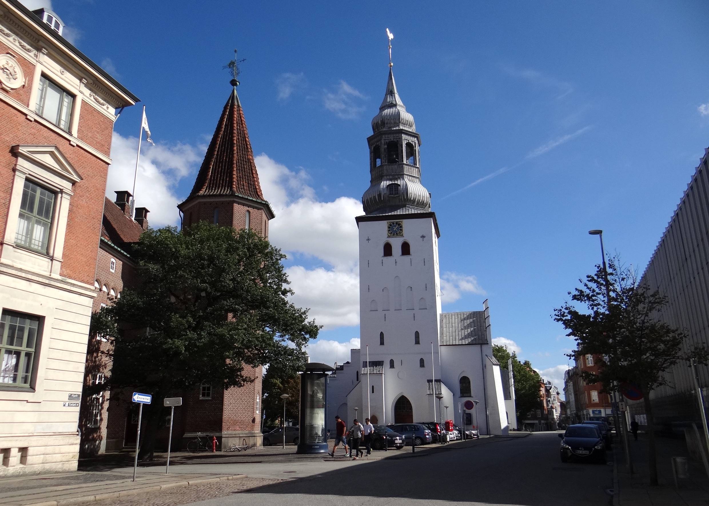 Straßenzug mit weißer Kirche am Ende, davor ein roter Backsteinturm