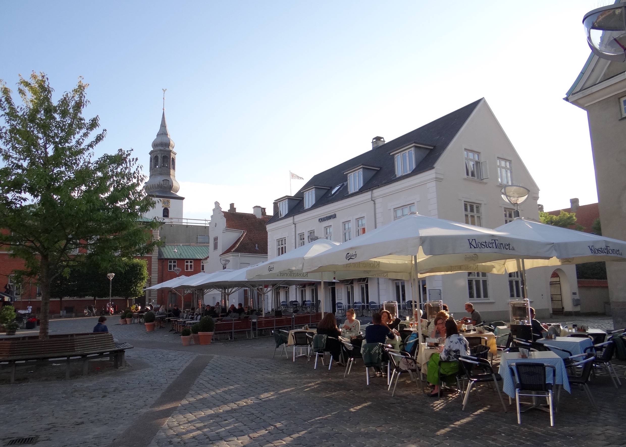 Außensitzplätze unter Sonnenschirmen vor einer Kirche in der Abendsonne