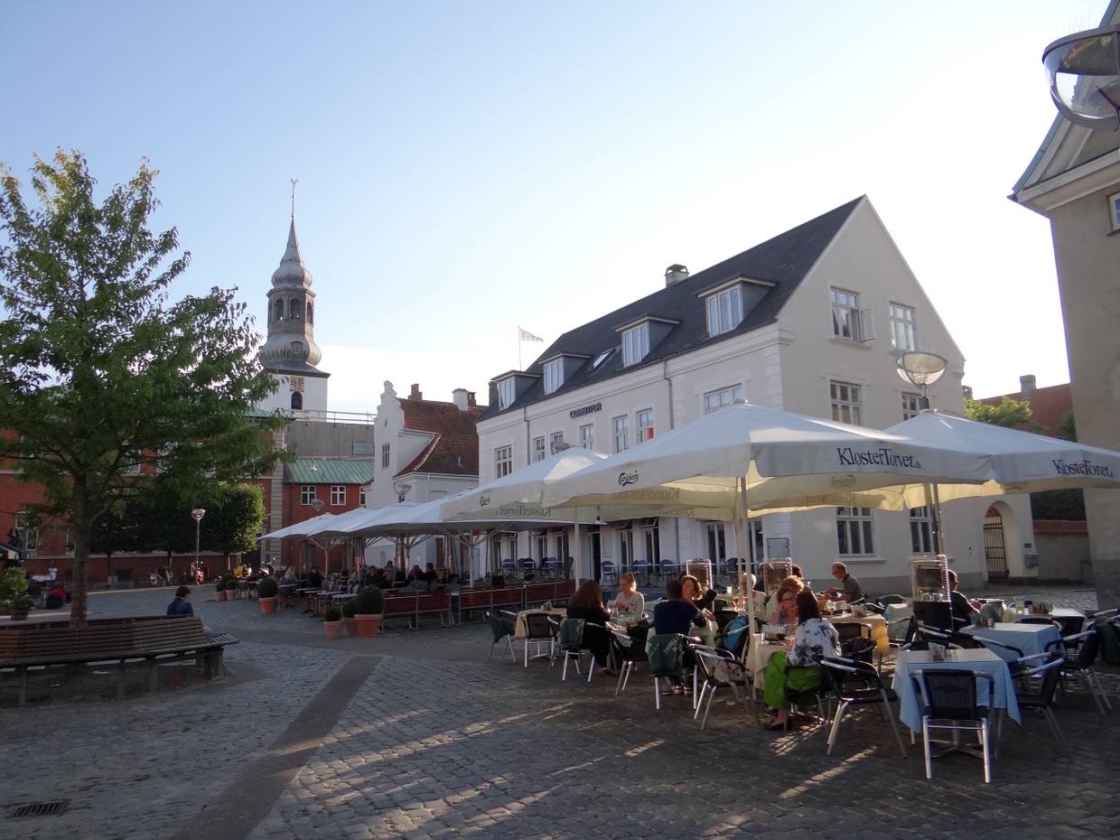 Außensitzplätze unter Sonnenschirmen vor einer Kirche in der Abendsonne
