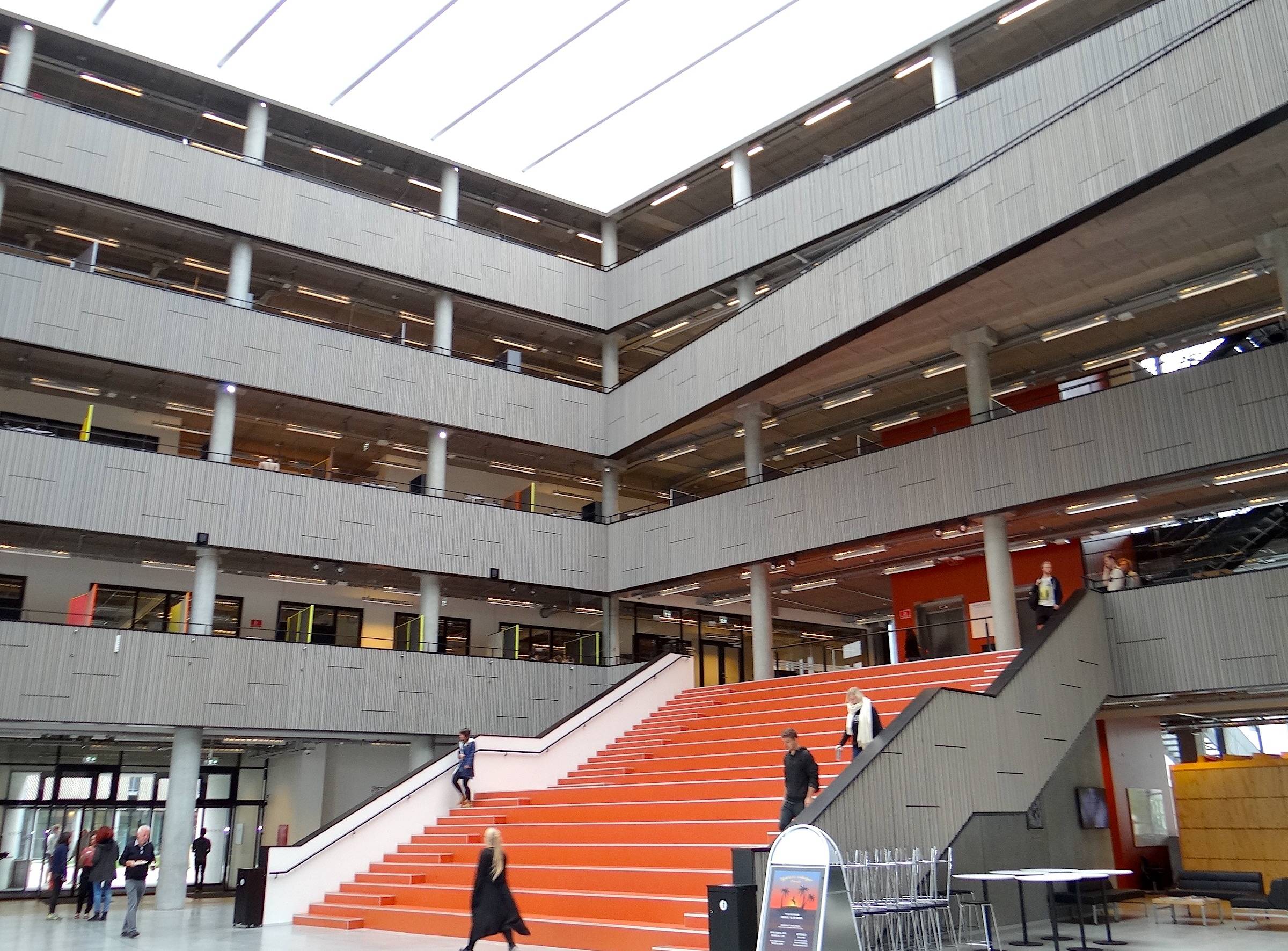 Eingangshalle mit offenen Balkonen über vier Etagen und einer breiten, roten Treppe