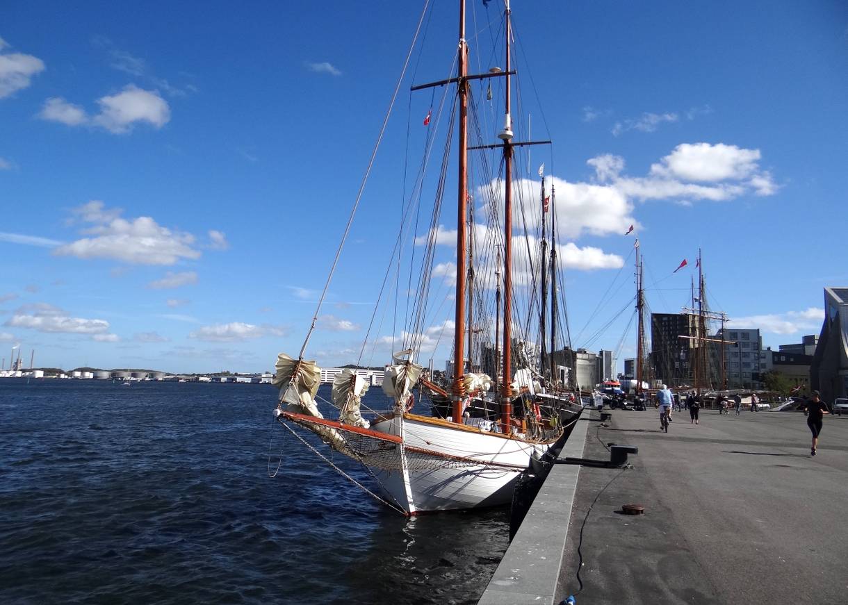 Die breite Uferpromenade mit einigen Passanten und historischen Segelschiffen an der Kaimauer