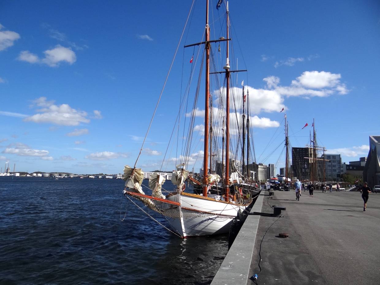 Die breite Uferpromenade mit einigen Passanten und historischen Segelschiffen an der Kaimauer