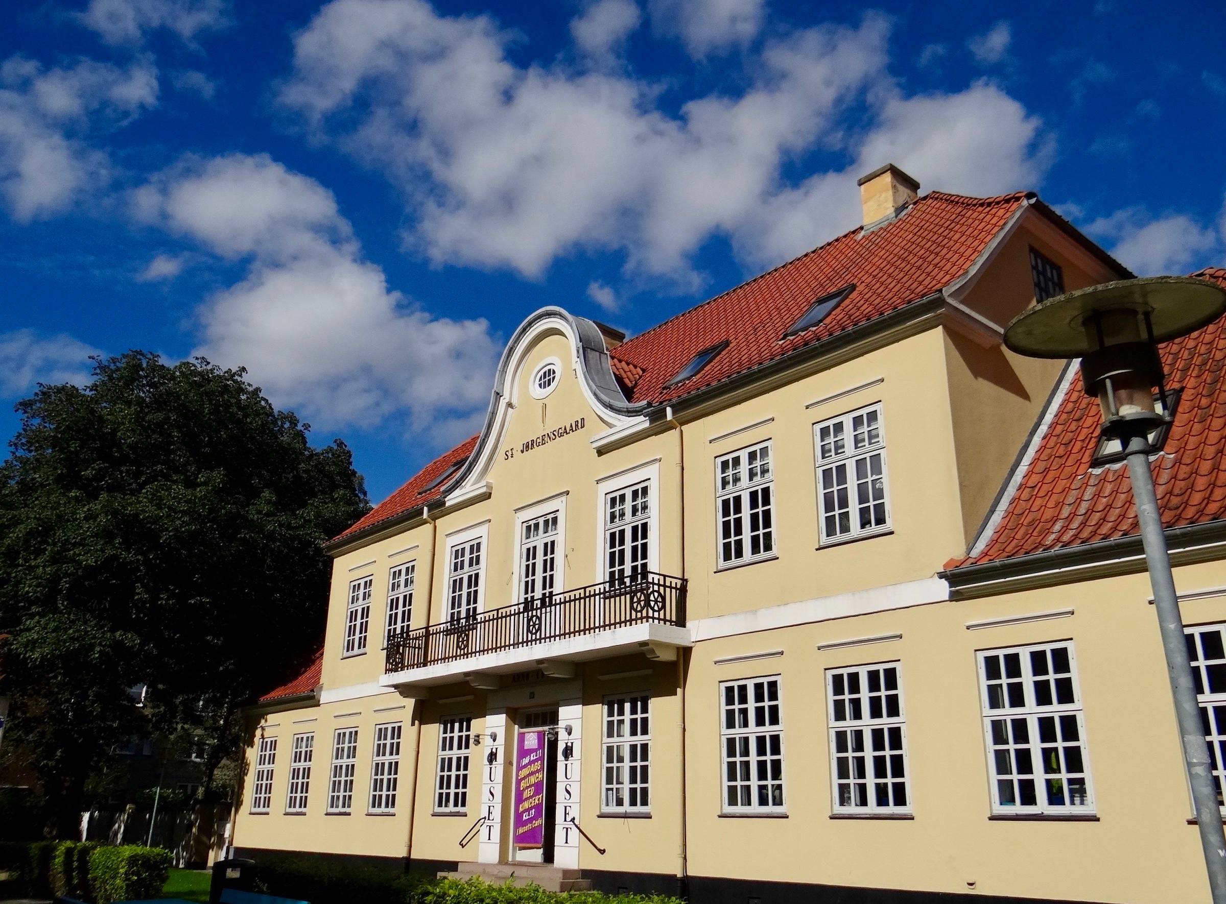 Gelbe Villa mit rotem Dach, am Eingang Werbung für eine Veranstaltung 