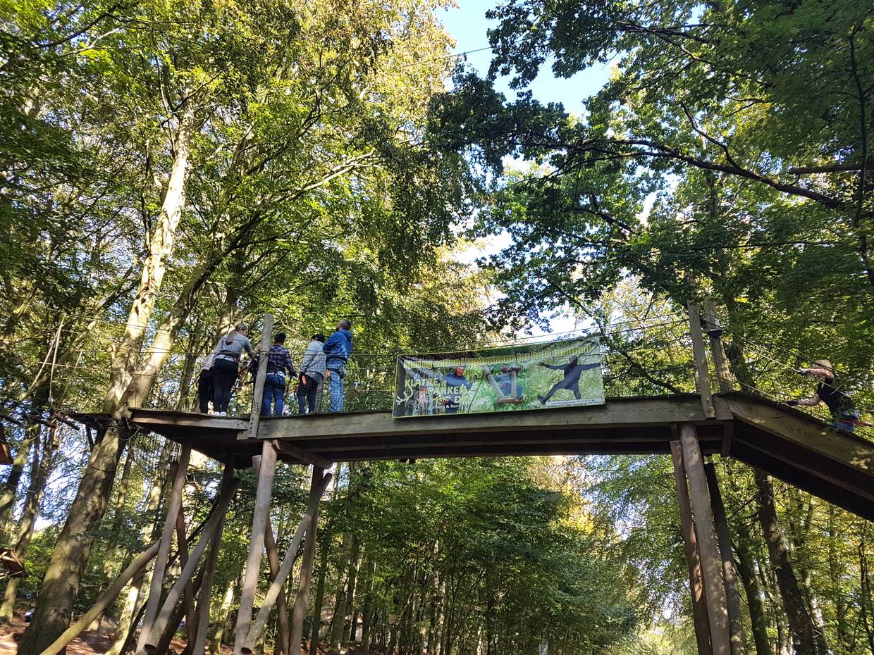 Holzbrücke zwischen den Bäumen, darauf Besucher des Kletterparks