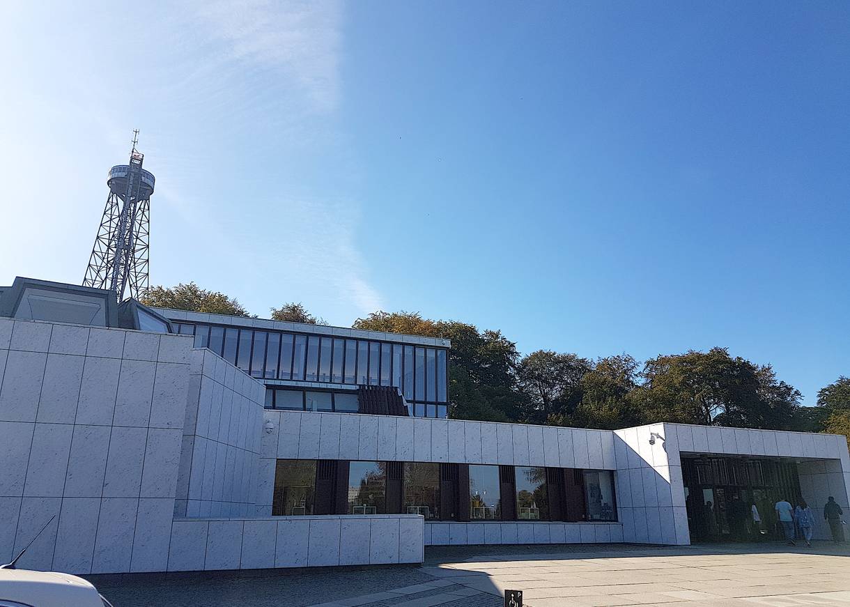 Gradliniger, moderner Bau, dahinter ragt ein Stahlturm auf