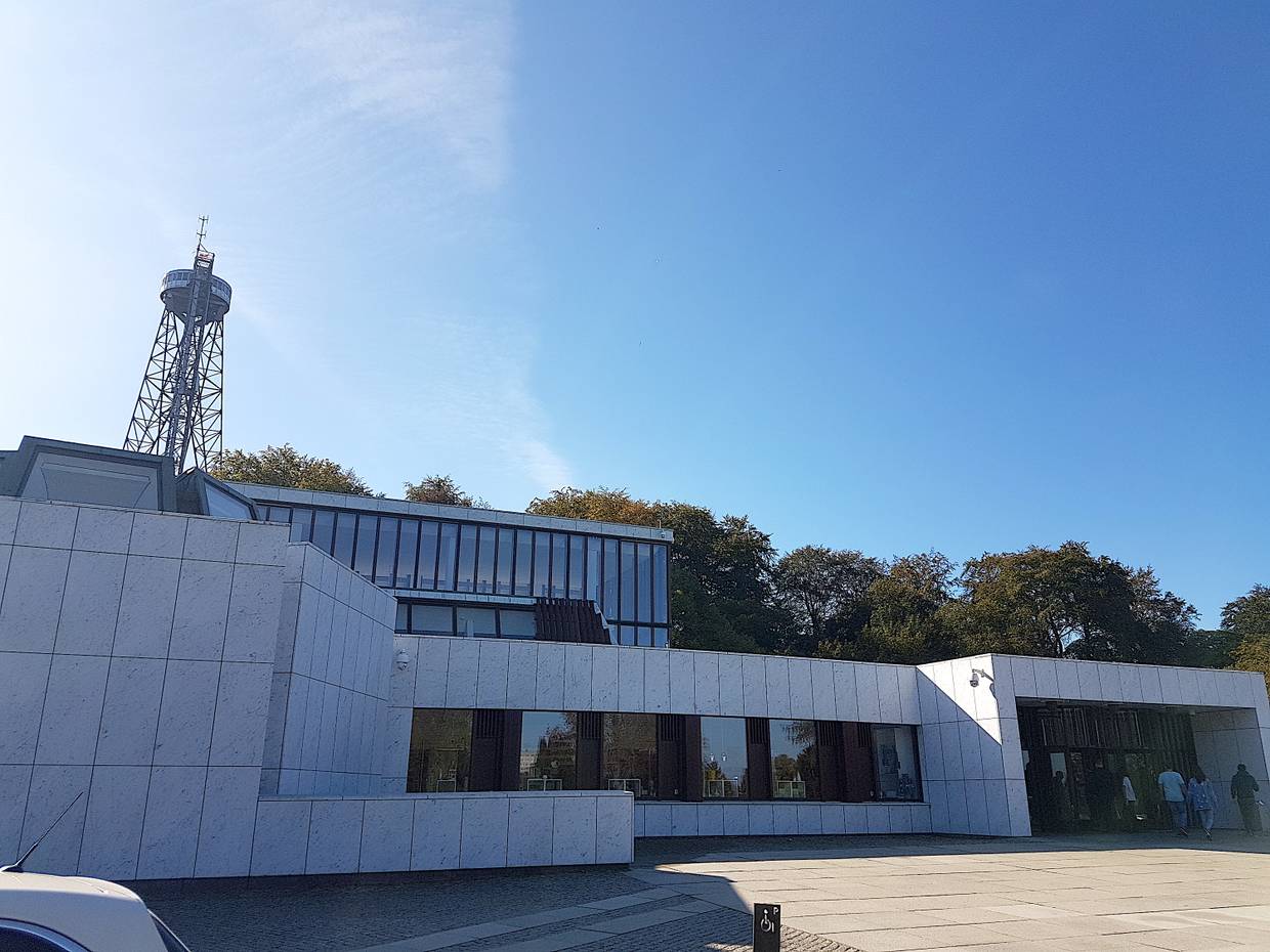 Gradliniger, moderner Bau, dahinter ragt ein Stahlturm auf