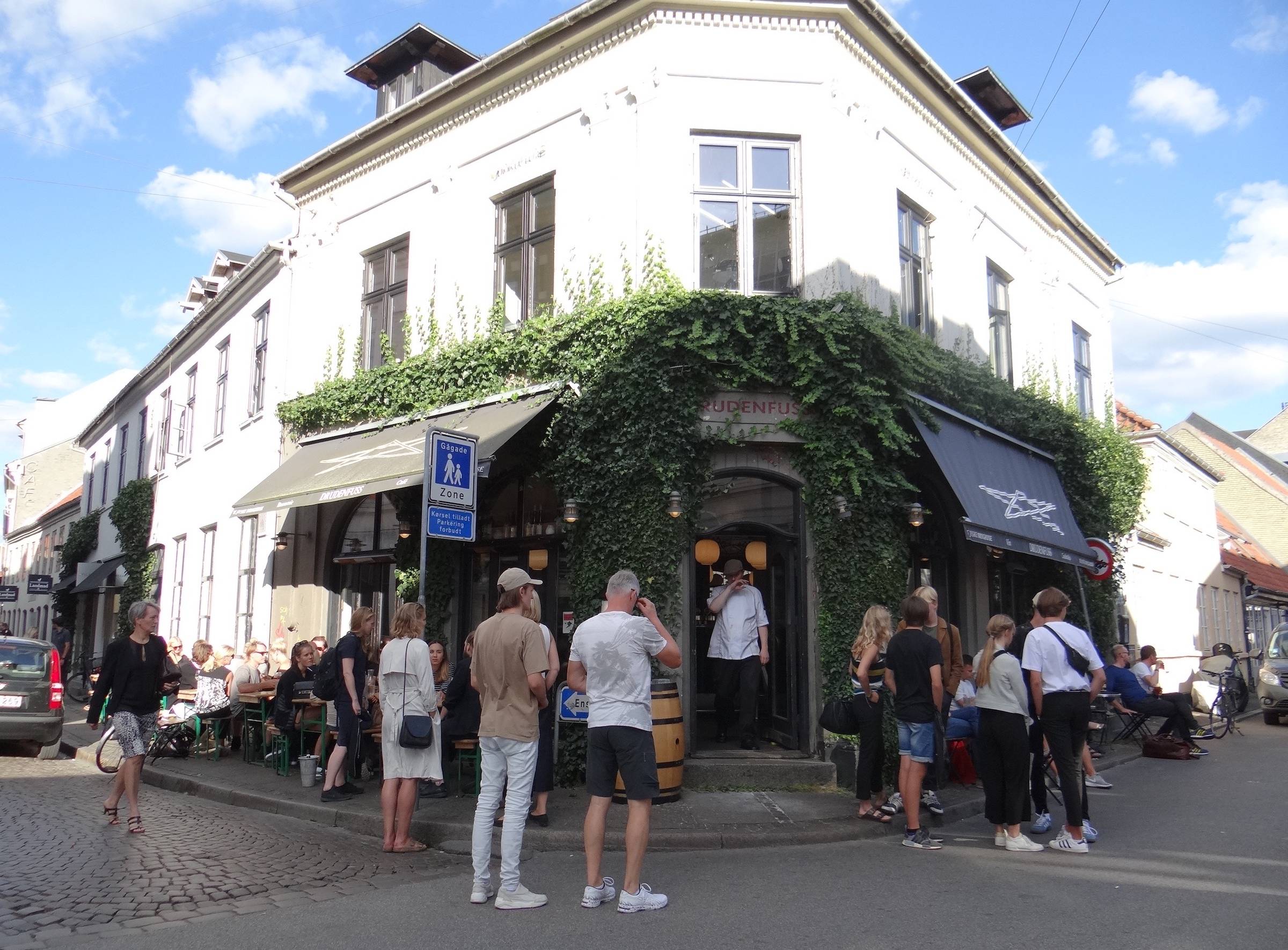Weißes Eckhaus mit einer Bar, viele Gäste vor der Tür