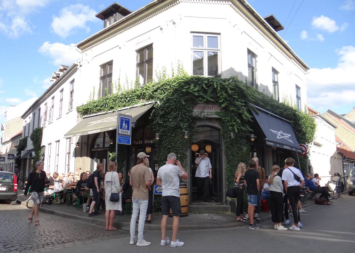 Weißes Eckhaus mit einer Bar, viele Gäste vor der Tür