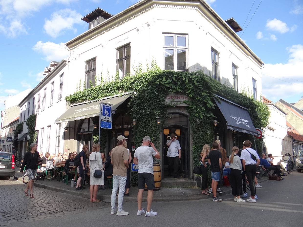 Weißes Eckhaus mit einer Bar, viele Gäste vor der Tür