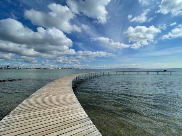 Blick über das Waaser. Im Vordergrund eine runde Holzbrücke, im Hintergrund ein größerer Hafen