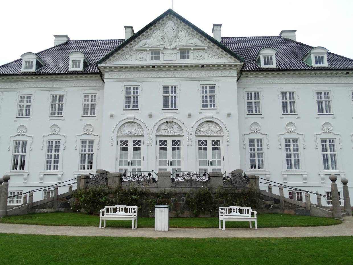 Weißes Herrenhäuser mit runden, reich verzierten Fensterbögen, davor zwei Bänke