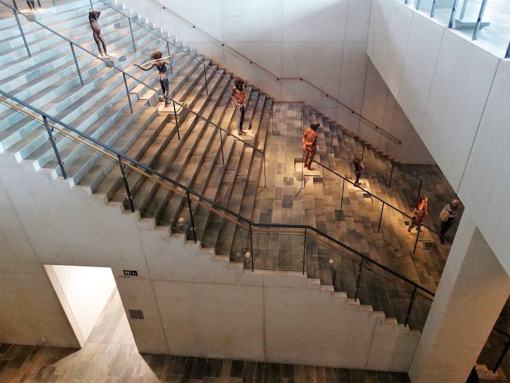 Breite Treppe im Inneren des Museums, in der Mitte Figuren von Menschen aus der Vorzeit
