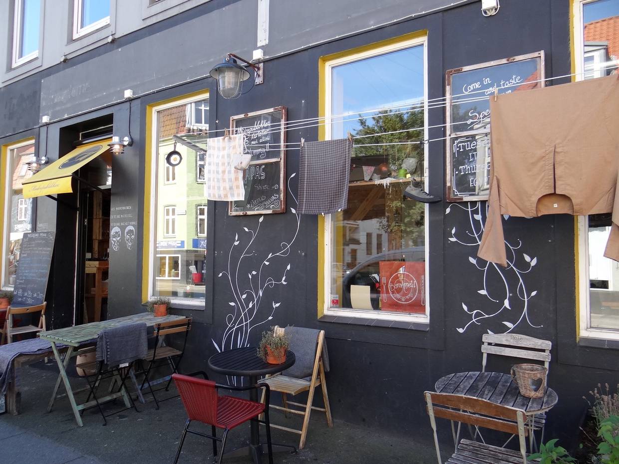 Fassade einer Pizzeria, die an eine Dorfszene in Italen erinnert, mit Wäsche an der Leine und unterschiedlichen, kleinen Tischen