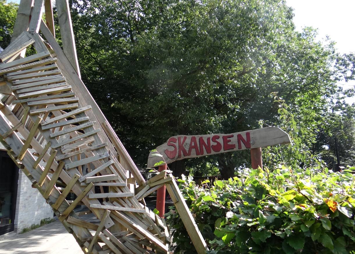 Handgezimmerte Treppe zwischen den Bäumen mit einem Holzschild, auf dem Skansen steht