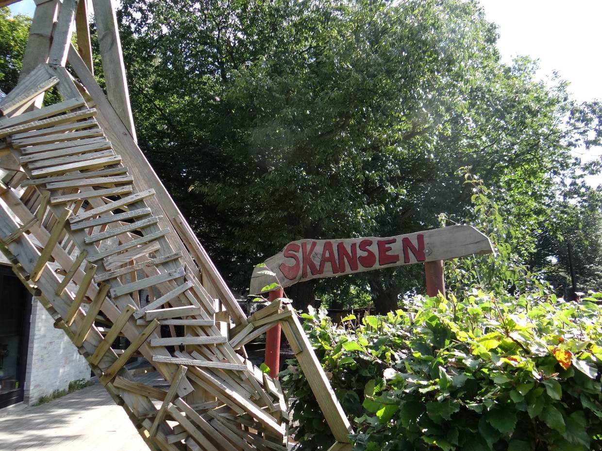 Handgezimmerte Treppe zwischen den Bäumen mit einem Holzschild, auf dem Skansen steht