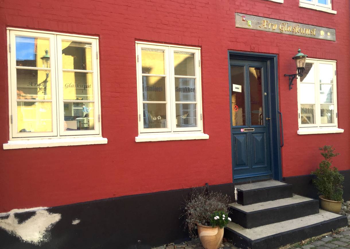 Ein rotes Wohnhaus mit weißen Fenstern, dunkelblaue Tür, Eingang zu einer Galerie
