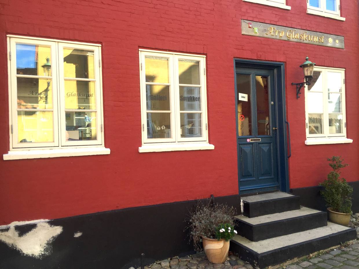 Ein rotes Wohnhaus mit weißen Fenstern, dunkelblaue Tür, Eingang zu einer Galerie