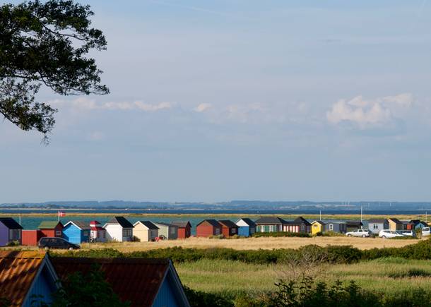 Blick auf eine lange Reihe farbiger Hütten am Meer zwischen einem Feld und dem Meer