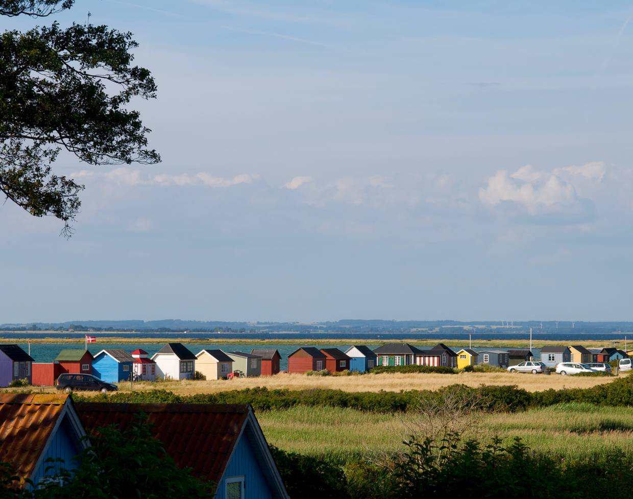 Blick auf eine lange Reihe farbiger Hütten am Meer zwischen einem Feld und dem Meer