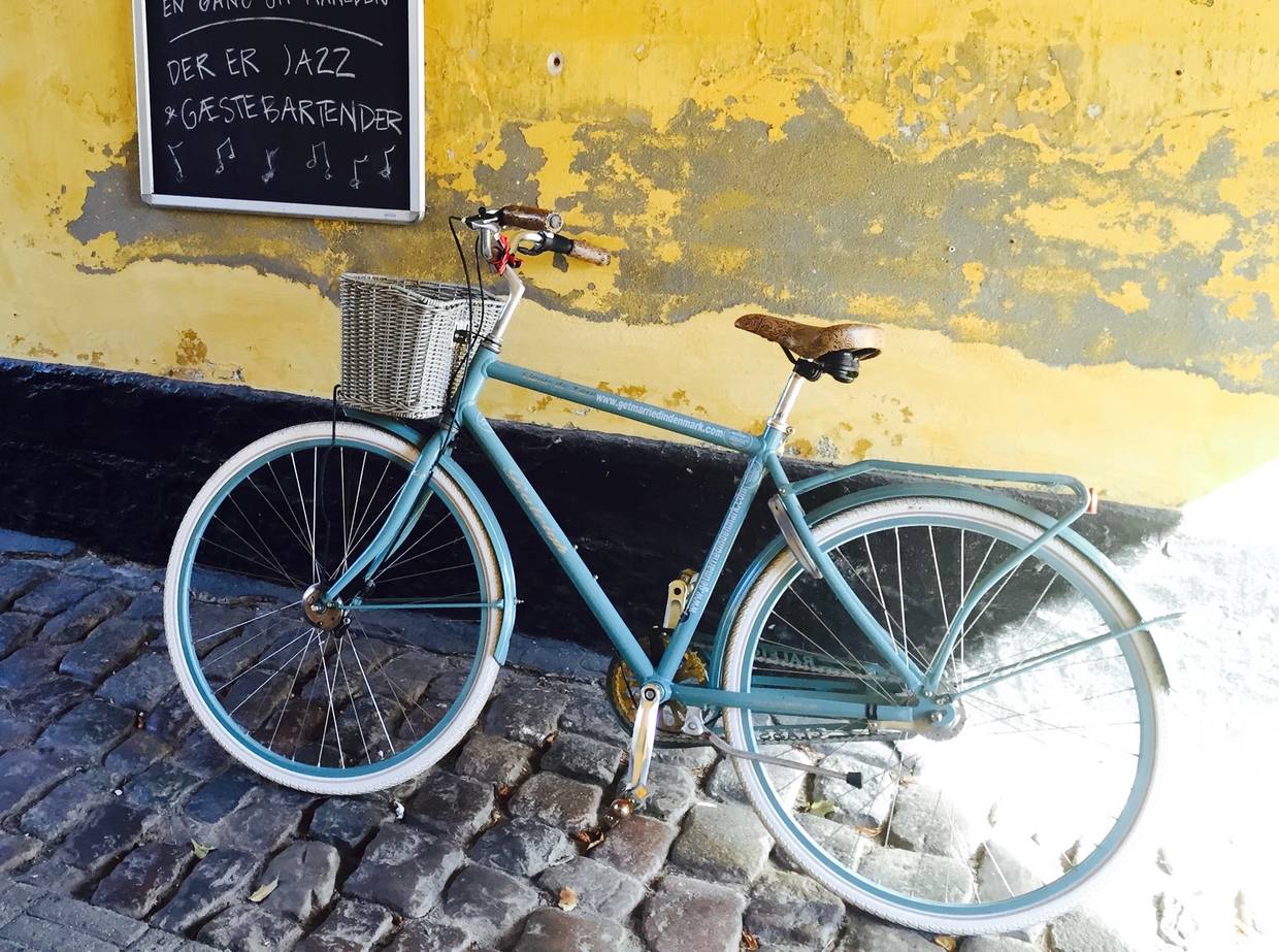 Altes blaues Fahrrad an gelber Wand mit Werbung für Hochzeit auf Ærø