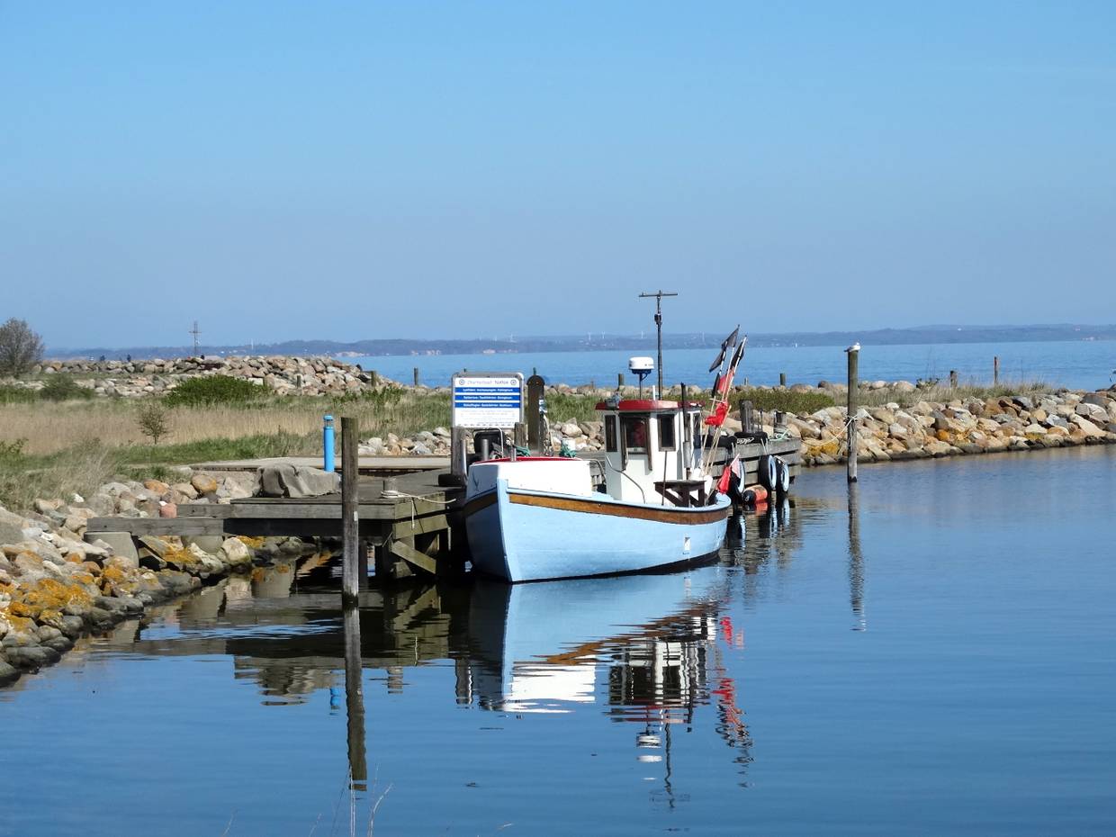 Blaues Fischerboot am Steg, umgeben von windstillem, blauen Wasser