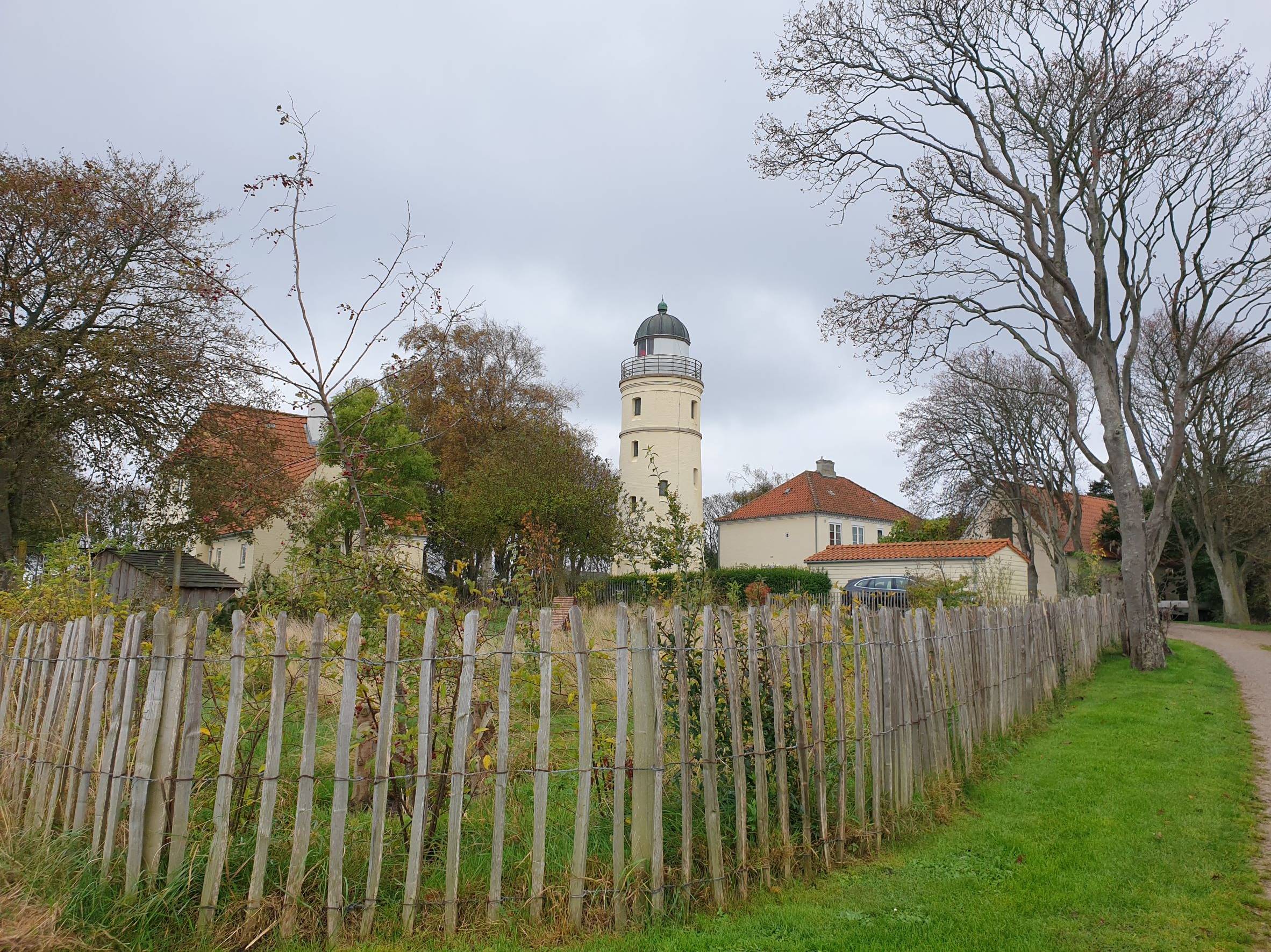 Blick über einen Holzzaun auf einen Garten und einen gelben Leuchtturm