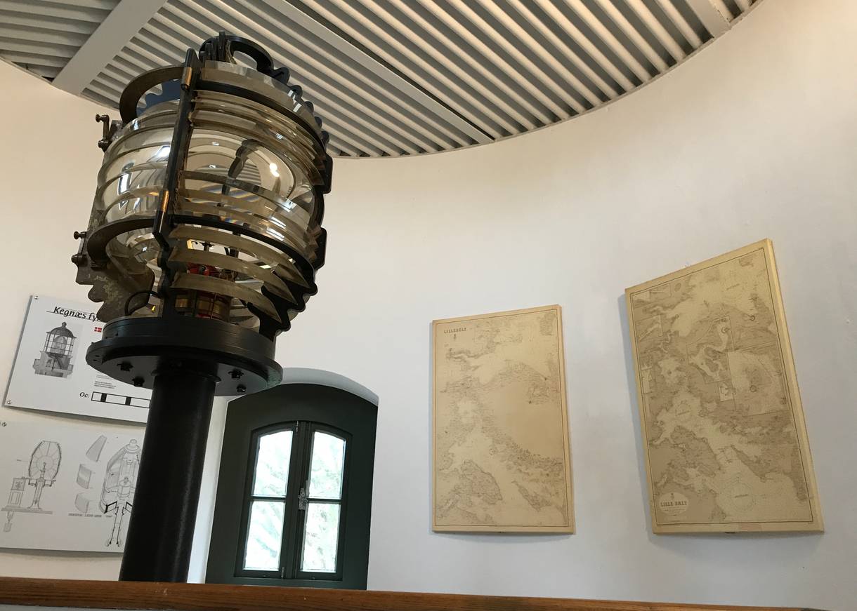 Blick ins Innere des Leuchtturms mit einer alten Lampe und Seekarten an den Wänden