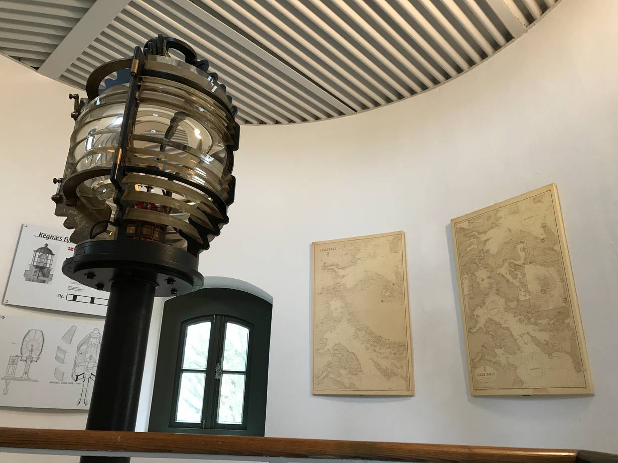 Blick ins Innere des Leuchtturms mit einer alten Lampe und Seekarten an den Wänden