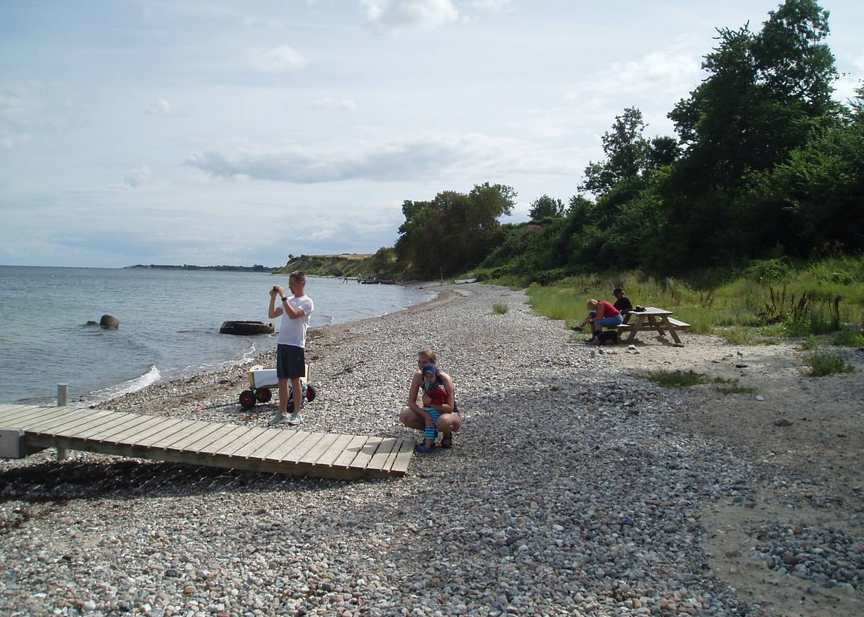 Familie auf einem steinigen Strandabschnitt, ein Badesteg ung Picknickbänke