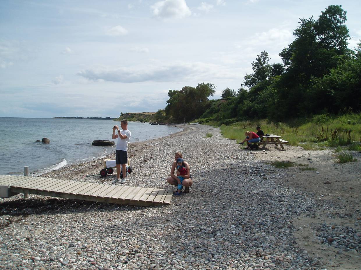Familie auf einem steinigen Strandabschnitt, ein Badesteg ung Picknickbänke