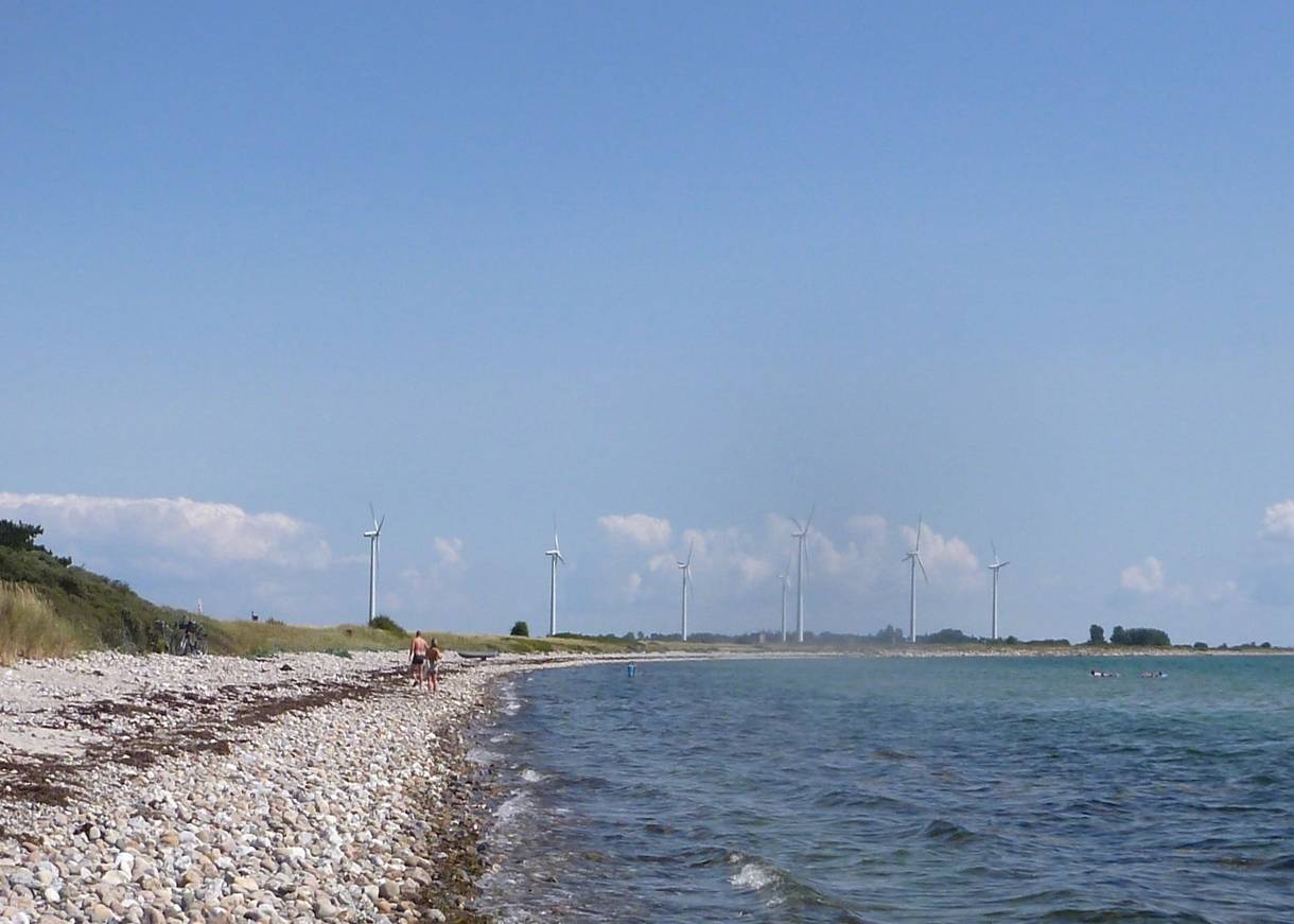 Steiniger, schmaler Strand, oim Hintergrund Windräder