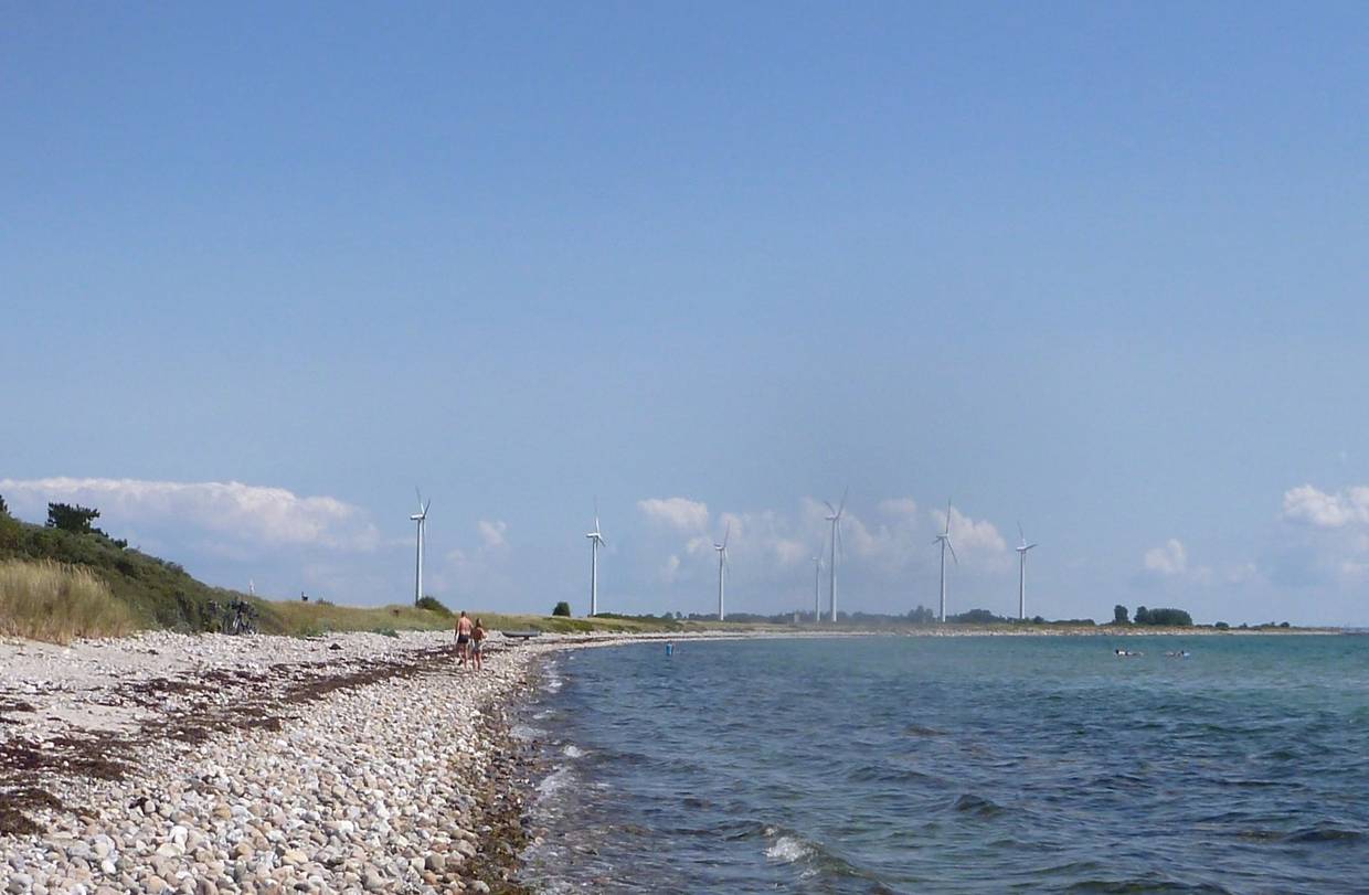 Steiniger, schmaler Strand, oim Hintergrund Windräder