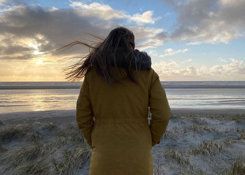 Frau mit dicker Jacke schaut aufs Meer