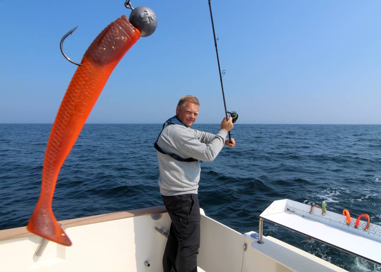 Angler wirft vom Boot eine Angel mit rotem Köder aus