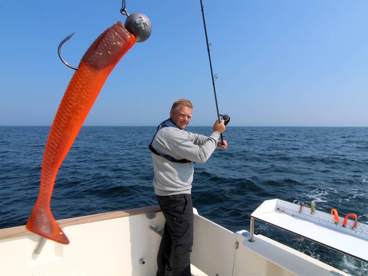 Angler wirft vom Boot eine Angel mit rotem Köder aus