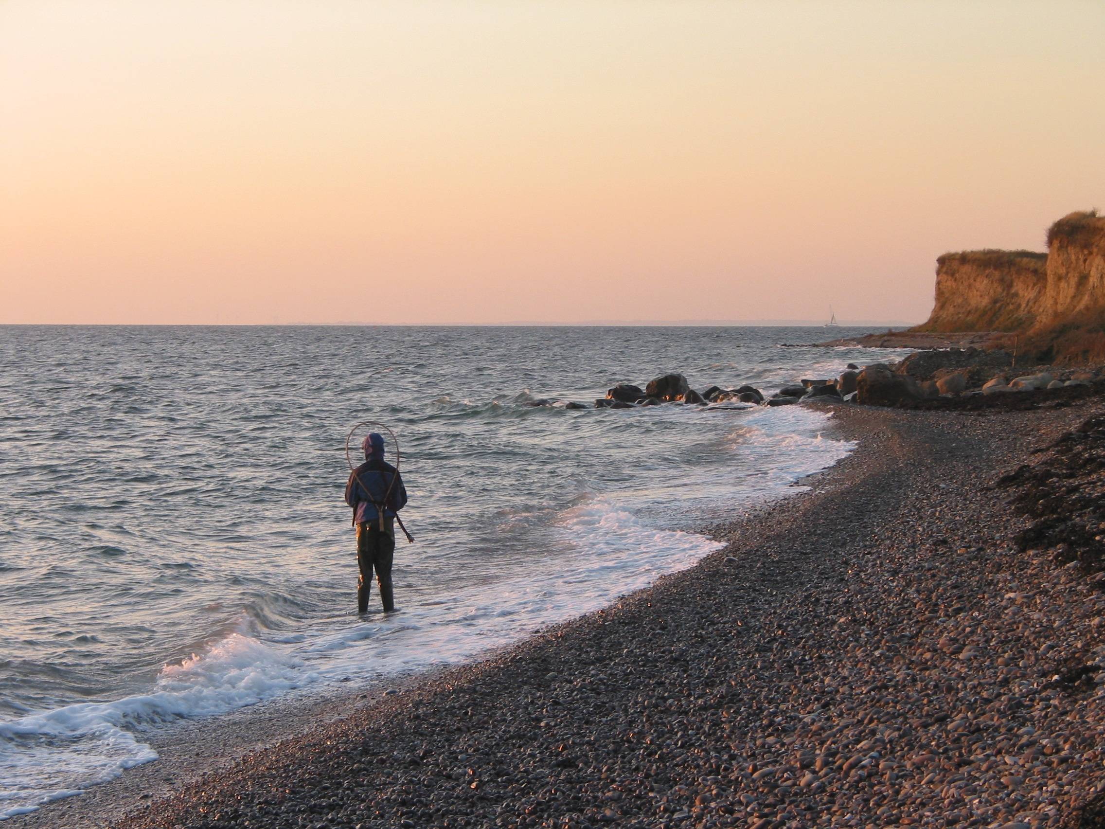 Angler im Wasser an einem Naturstrand mit Steinen