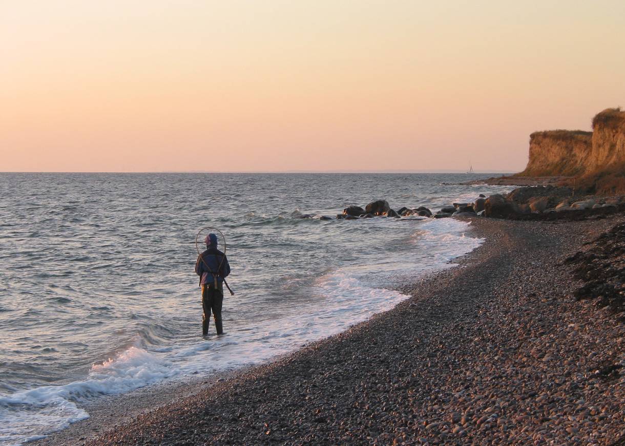 Angler im Wasser an einem Naturstrand mit Steinen