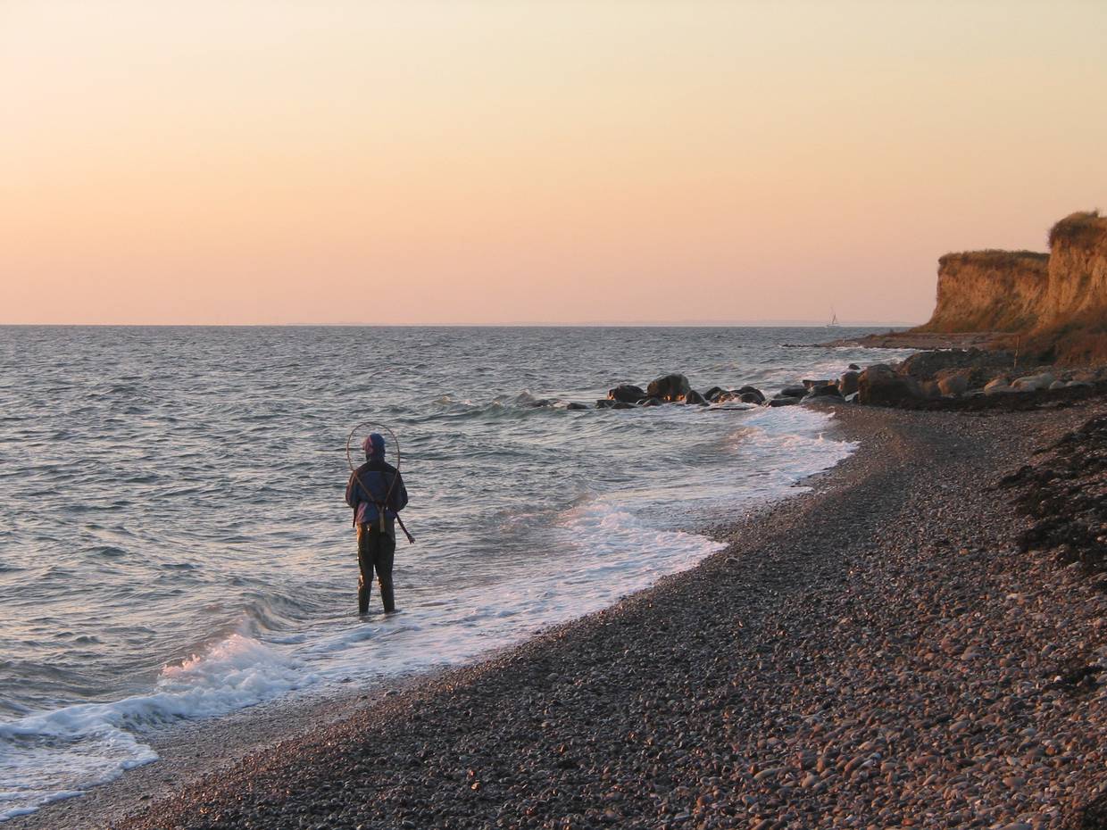 Angler im Wasser an einem Naturstrand mit Steinen