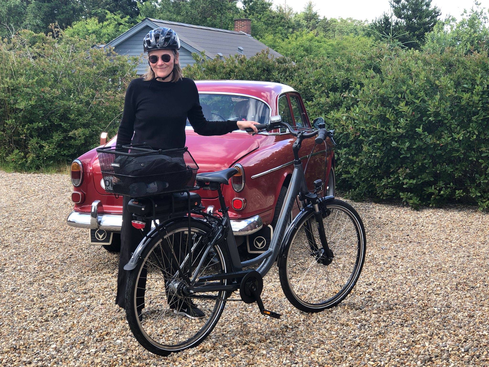 Frau mit Fahrrad und Helm vor einem alten Auto