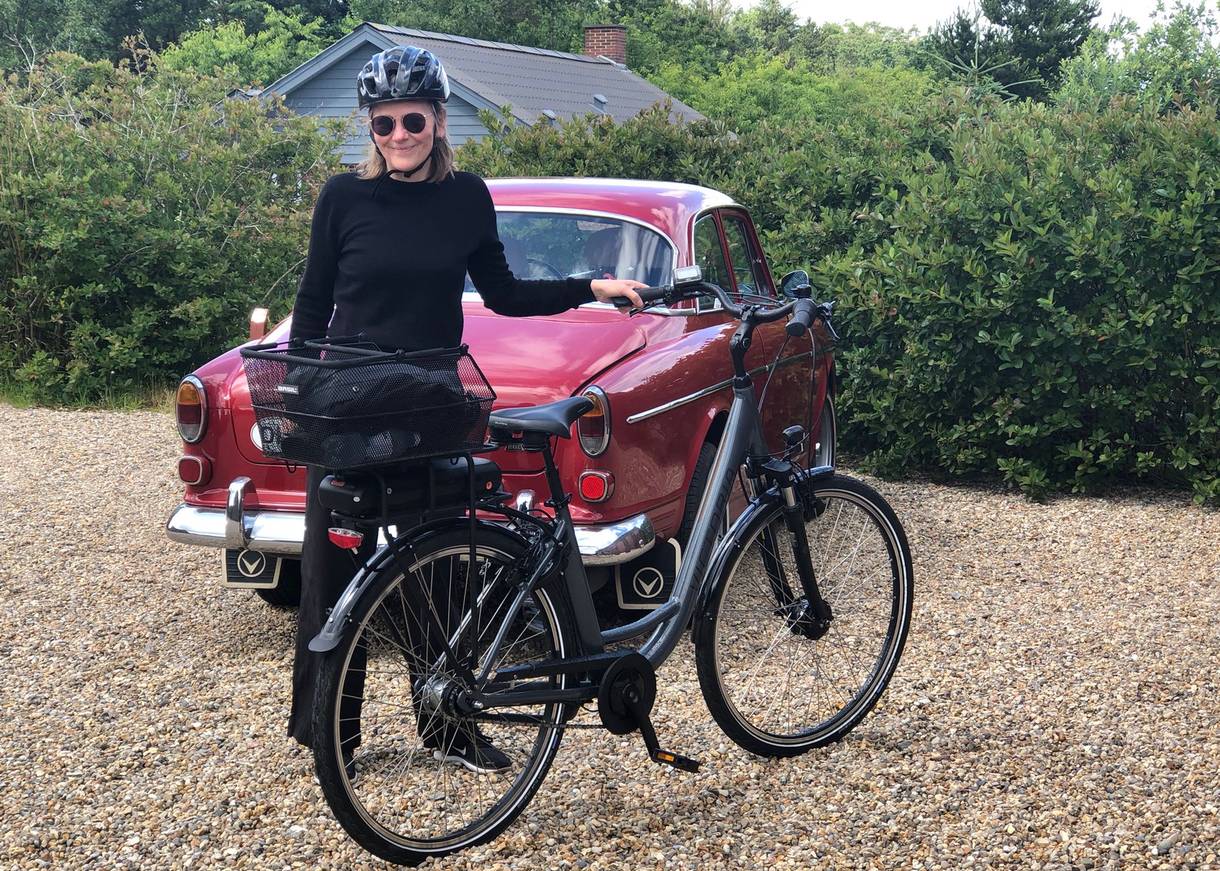 Frau mit Fahrrad und Helm vor einem alten Auto