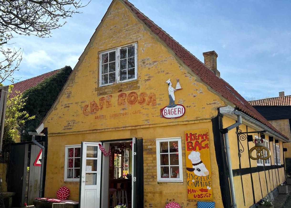 Blick auf Fassade eines kleines, gelbes Steinhaus mit einem bunten Café