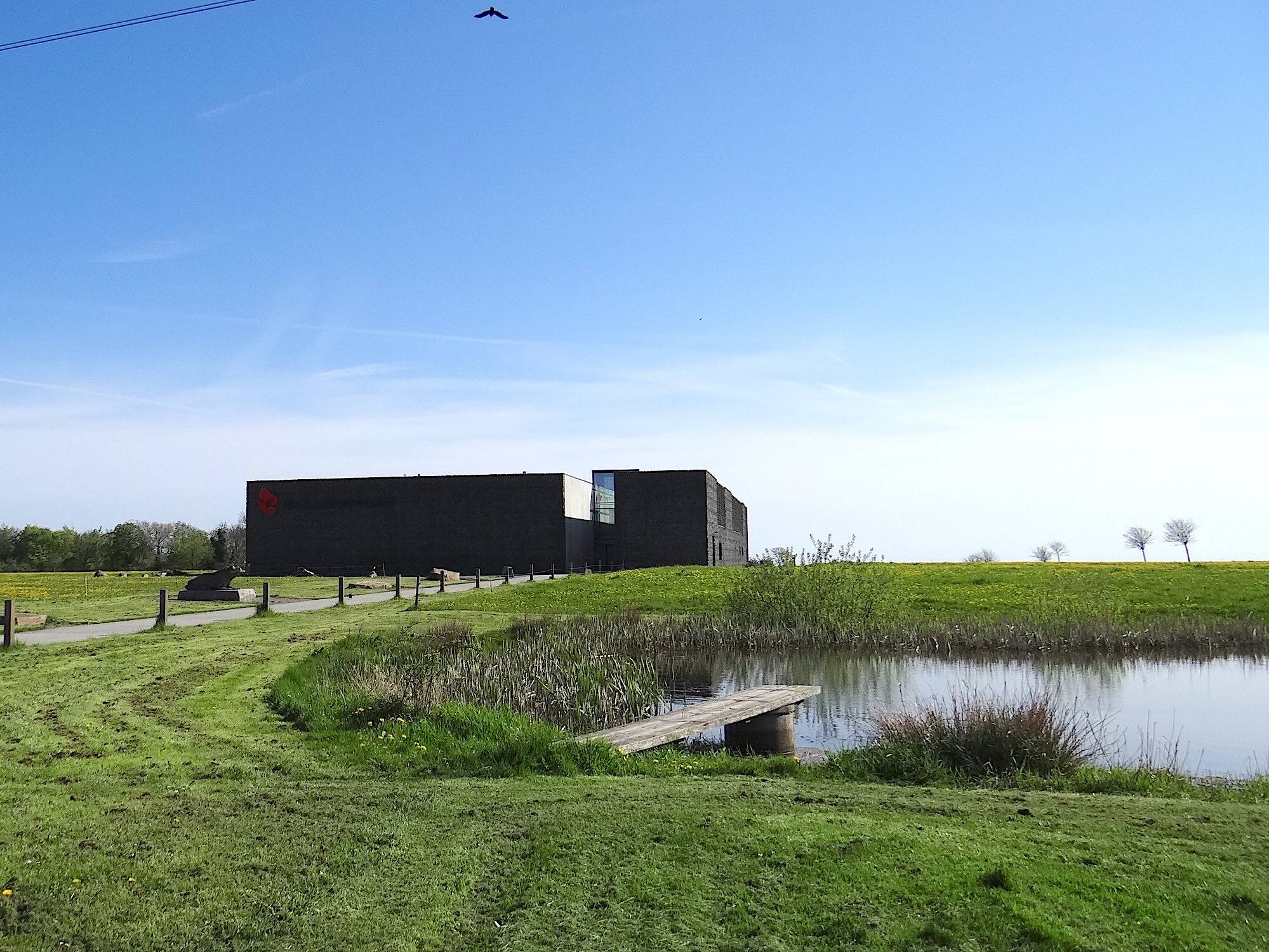 Schwarzer, flacher Neubau auf einer Wiese, davor ein Teich