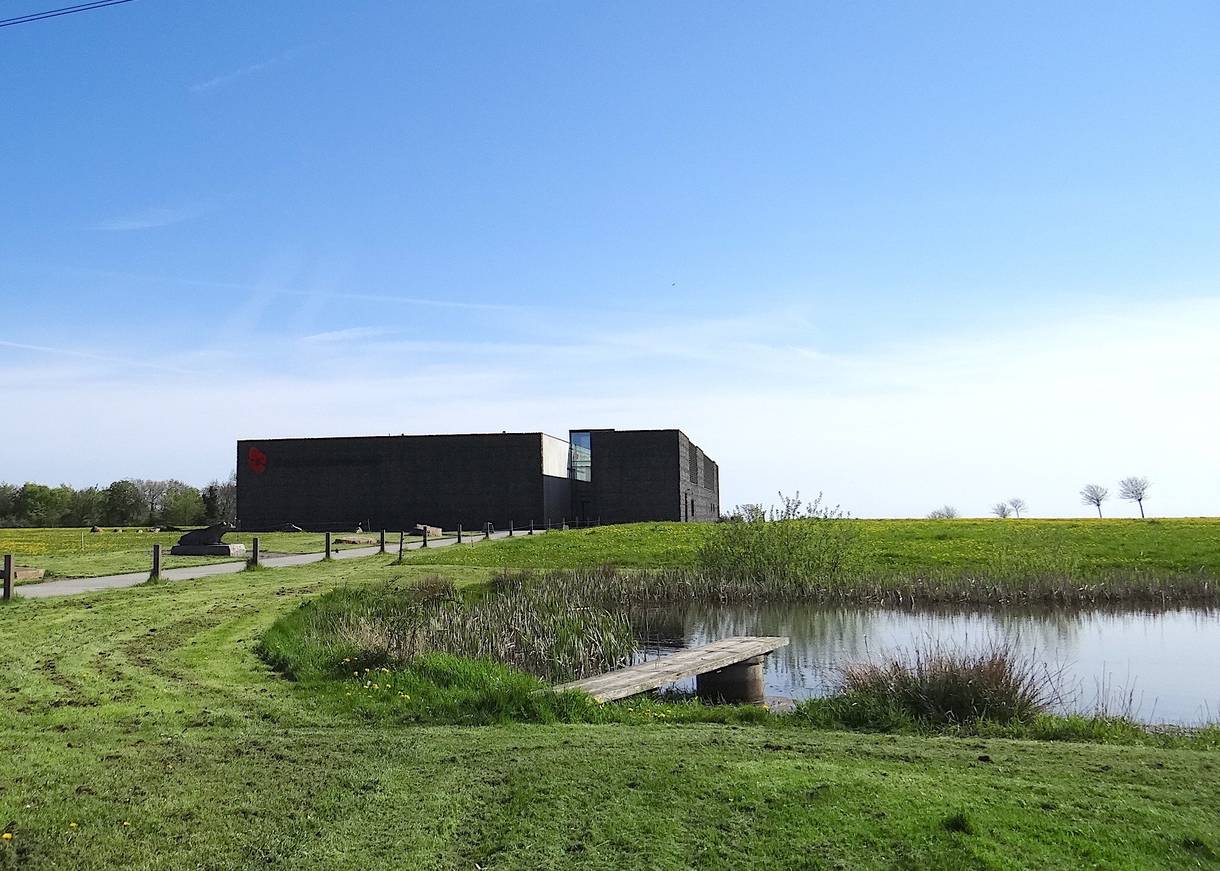 Schwarzer, flacher Neubau auf einer Wiese, davor ein Teich