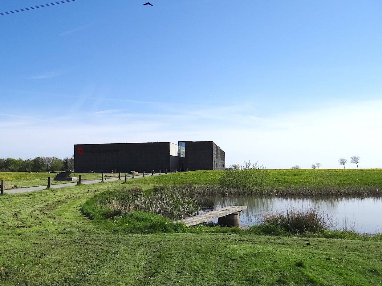 Schwarzer, flacher Neubau auf einer Wiese, davor ein Teich