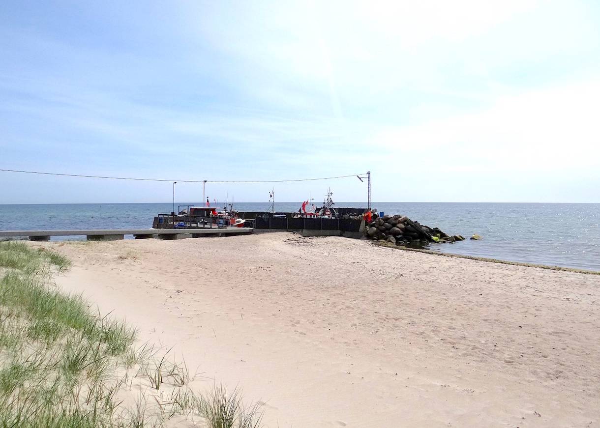 Sandstrand, dahinter ein kleiner, vorgelagerter Hafen