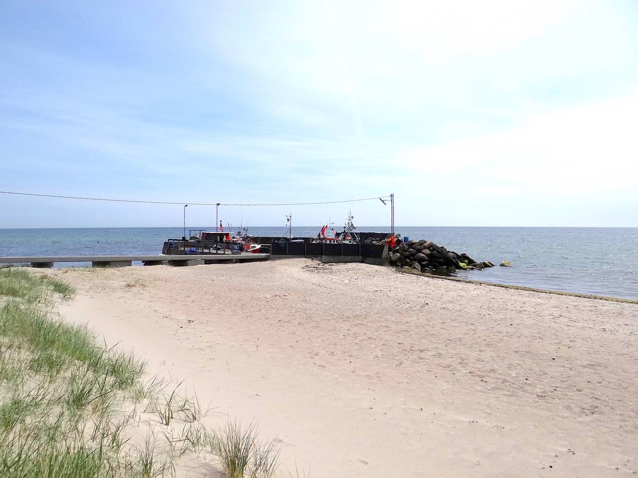 Sandstrand, dahinter ein kleiner, vorgelagerter Hafen