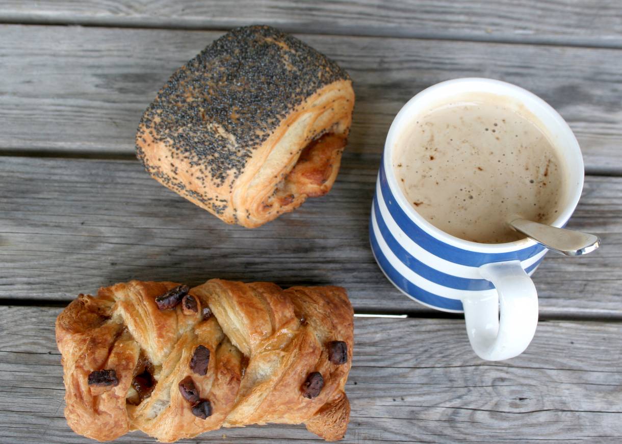 Kaffetasse und zwei Blätterteigstückchen auf einer Holzbank
