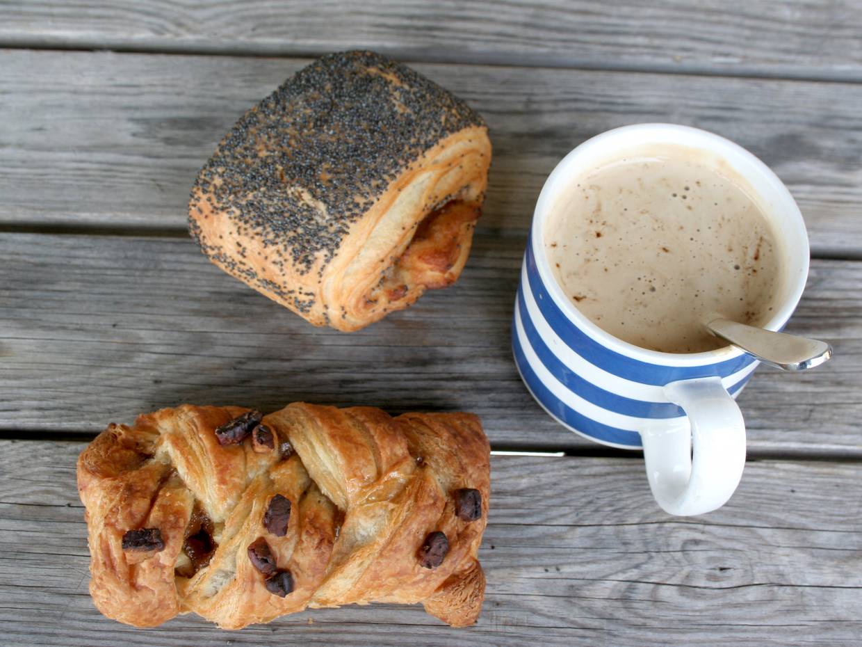 Kaffetasse und zwei Blätterteigstückchen auf einer Holzbank