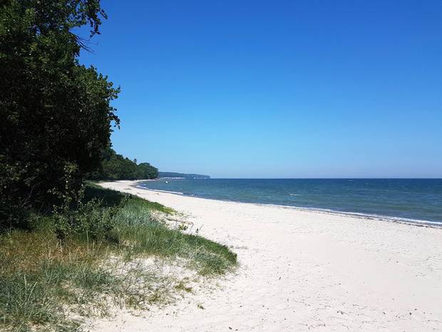 Menschenleerer weißer Sandstrand mit Wald links uns blaues Meer rechts