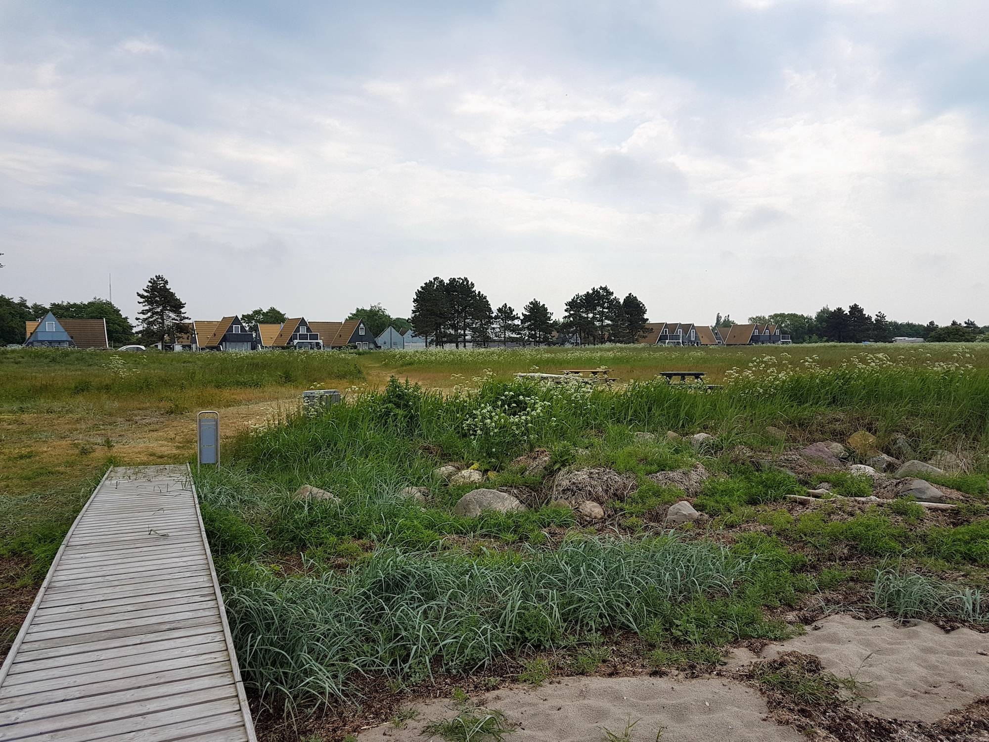 Kleine Nurdachhäuser hinter einer Wiese am Meer